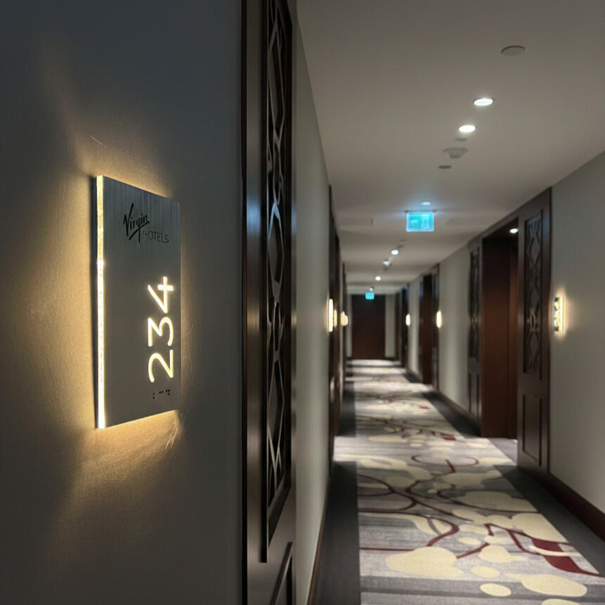 ADA compliant Braille hotel room number sign mounted on a modern hotel door Hotel door number plaque with ADA compliant Braille and brand logo